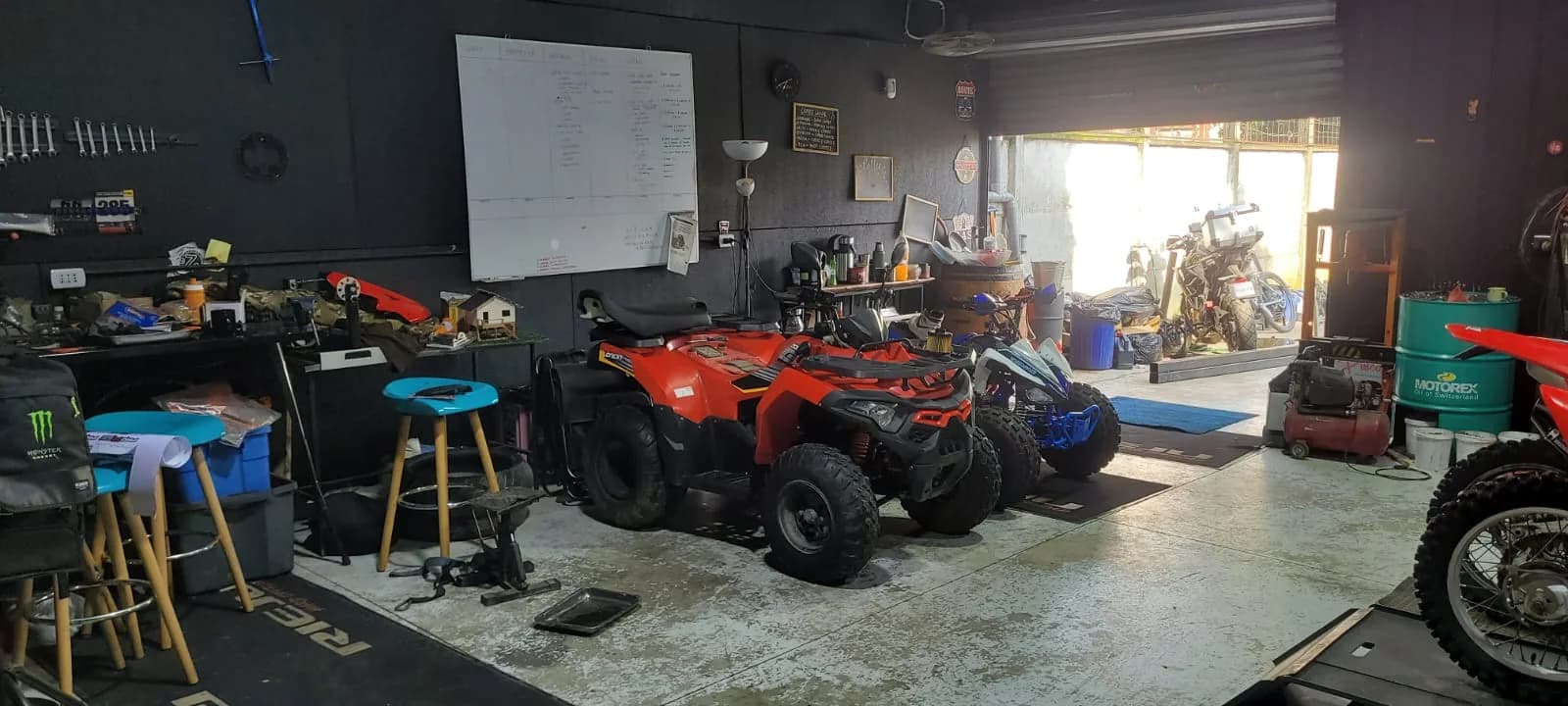 Sector del taller de Proride con dos cuatrimotos en mantención, el portón abierto y la planilla de trabajos en el muro